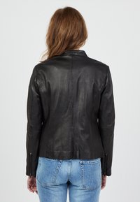 Zwarte leren jas met een slimfit ontwerp, rechte rugnaad en ritsmanchetten. Draagt over lichtgewassen denim jeans. Gladde, glanzende textuur.