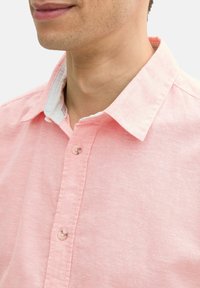 Lichtroze linnen shirt met een knoopsluiting, contrasterende witte kraag en een zachte textuur. Heeft knopen aan de voorkant.