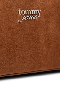 Καφέ ύφασμα σουέντ με ασημένιο μεταλλικό λογότυπο "tommy jeans" στο πάνω κέντρο, μέρος ρούχου ή αξεσουάρ.