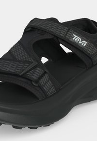 Μαύρο σανδάλι Teva με χοντρή σόλα και ρυθμιζόμενους ιμάντες με σχέδια πάνω από το πόδι και γύρω από τον αστράγαλο.