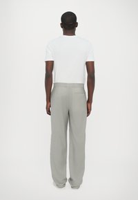 Pelēki plaša piegriezuma bikses ar gludu tekstūru, ar aizmugures kabatu, kombinētas ar vienkāršu baltu T-kreklu. Neitrālas sneakers noslēdz rezultātu.