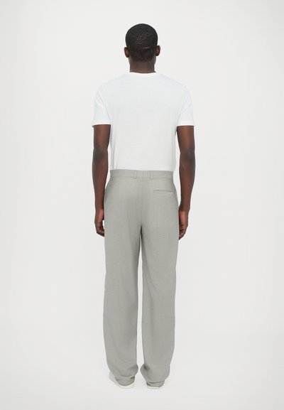 Γκρι παντελόνια με φαρδιά εφαρμογή και λεία υφή, με πίσω τσέπη, σε συνδυασμό με ένα απλό λευκό μπλουζάκι. Ουδέτερα sneakers ολοκληρώνουν την εμφάνιση.