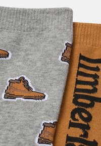 Calzini grigi e marroni con un motivo a stivale su uno, con la parola "Timberland" in nero sulla sezione arancione, che mostra una consistenza a maglia.