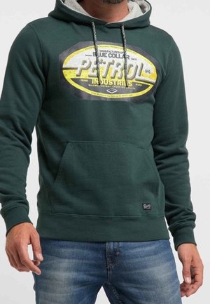 Vihreä huppari, jossa on harmaa vuori, ja jonka etuosassa on suuri keltainen ja musta graafinen logo "PETROL INDUSTRIES" sekä etutasku.