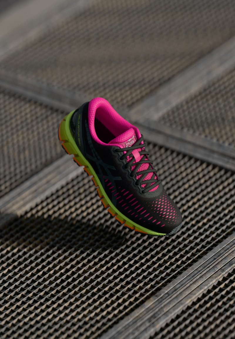 Svart løpesko med rosa innside og grønn såle på metallristoverflate utendørs i dagslys.