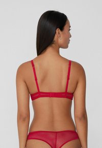 Red lace bra with adjustable straps, sheer material, and a hook-and-eye back closure, paired with matching red minimalist underwear.