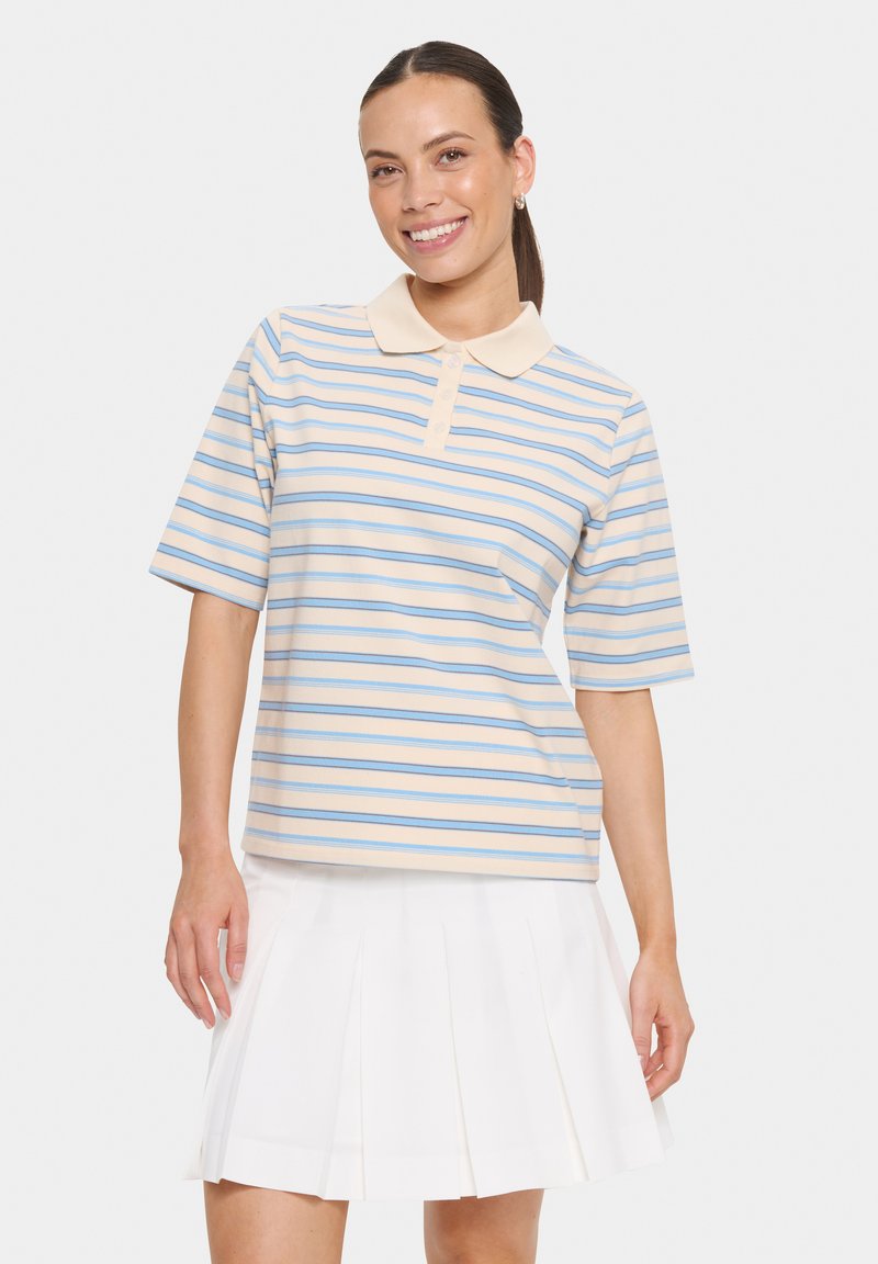Polo à rayures beige et bleu clair, en tissu doux, avec un col pointu et des manches courtes. Associé à une jupe blanche plissée.