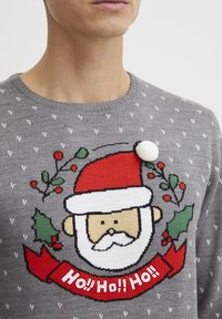 Pull en tricot gris orné d'un graphique de Père Noël, portant un chapeau rouge et une barbe blanche, avec une banderole "Ho !! Ho !! Ho !!". Motifs de flocons de neige blancs partout.