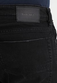 Svarta denimjeans med en läderlapp som har texten "DIESEL," med standard bakfickor och kontrasterande sömmar.