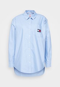 Light blue long-sleeve button-up shirt in cotton with a rounded hem. Features a patch pocket and logo on the left chest. Standard collar.