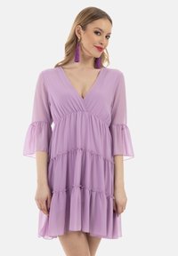 Lilafarbene Kleid mit V-Ausschnitt, transparentem Stoff, ausgestellten Ärmeln und gestuftem Rüschendesign. Akzentuiert mit gerafften Details für zusätzliche Textur.
