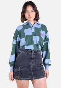 Chemise à manches longues avec col dans un motif à carreaux vert et bleu clair, associée à une jupe en jean noire taille haute avec poches et broderies.