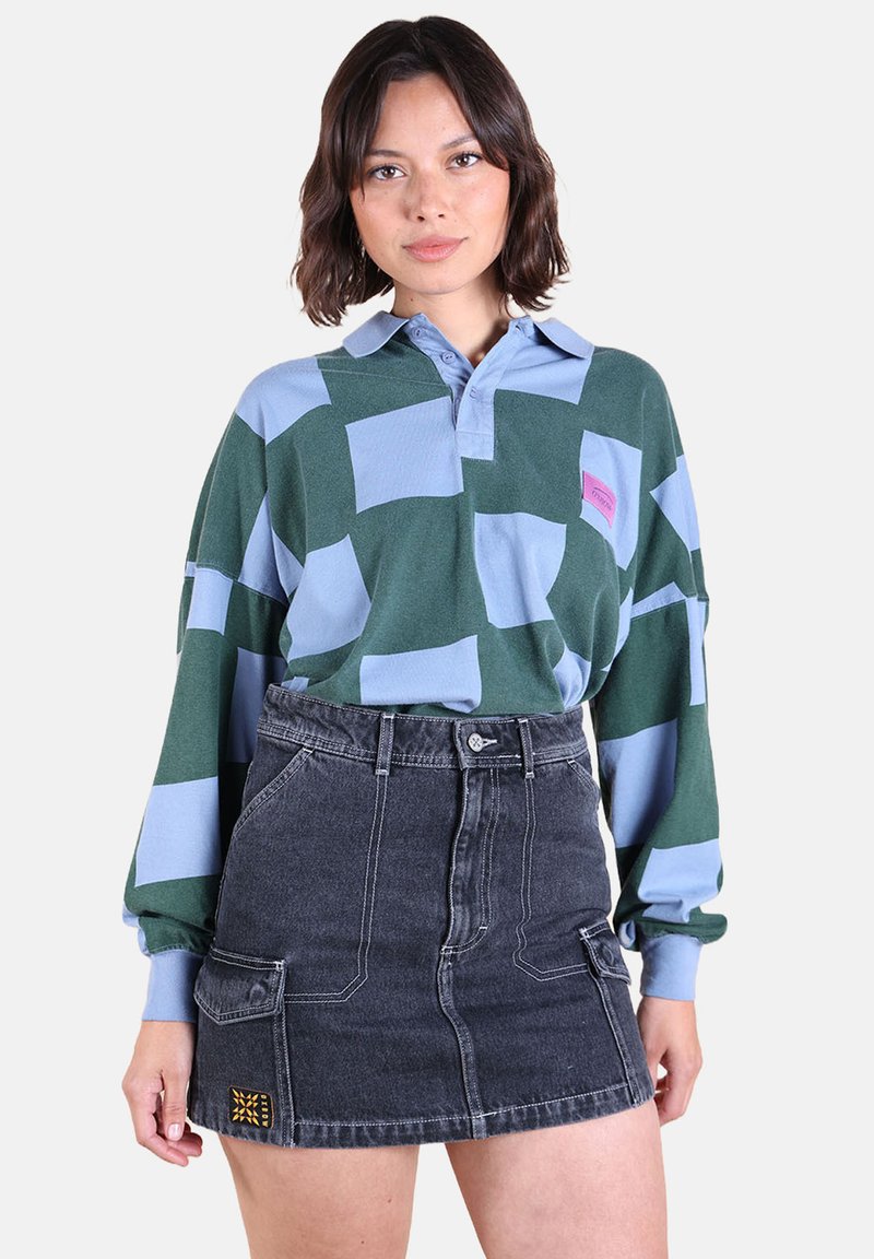 Chemise à manches longues avec col dans un motif à carreaux vert et bleu clair, associée à une jupe en jean noire taille haute avec poches et broderies.