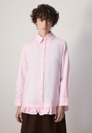 Lys pink skjorte med lange ærmer, der har en flæse i bunden. Simpelt krave og knappet front. Glat stof tekstur.