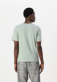 Lys grønn bomull t-skjorte med rund hals og korte ermer, paret med grå jeans. Glatt tekstur og standard passform.