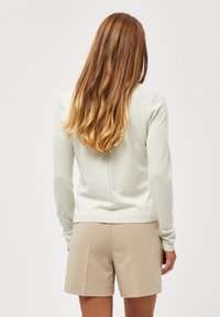 Ljusgrön stickad tröja med långa ärmar, med en subtil sömdetalj bak, parat med beige skräddarsydda shorts.