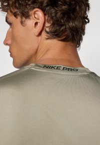 Nike Pro sportpóló, olívazöld, testhezálló dizájn, sima textúra, kontrasztos fekete márkázással a hát nyakvonalán és diszkrét varrással.