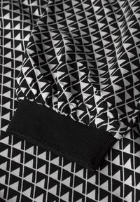 Schwarz-weißes Gewebe mit einem geometrischen Dreiecksmuster, versehen mit einem strukturierten schwarzen Bündchen und gerafftem Stoff für zusätzlichen Schwung.