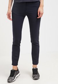 Námořnické slim fit kalhoty s hladkou texturou, zdobené bočními akcenty. V kombinaci s černými a vzorovanými sportovními botami.