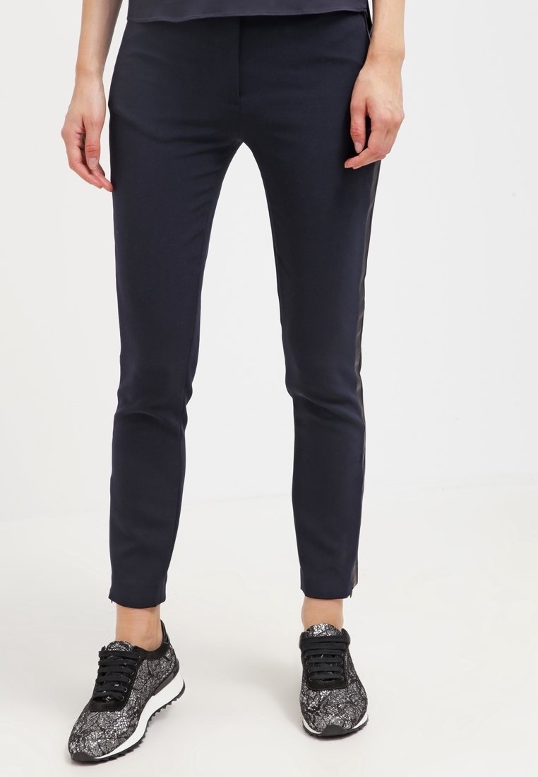 Námořnické slim fit kalhoty s hladkou texturou, zdobené bočními akcenty. V kombinaci s černými a vzorovanými sportovními botami.