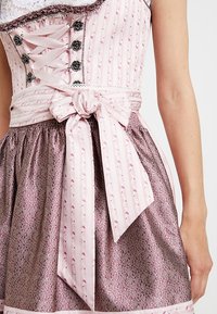 Abito dirndl rosa e decorato con un corsetto attillato caratterizzato da dettagli con lacci, accenti floreali e una gonna arricciata di tonalità più scura.