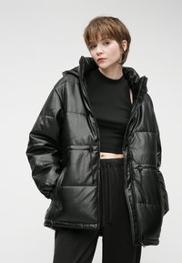 Čierna zateplená bunda s lesklou, hladkou textúrou, nastaviteľnou kapucňou a šnúrkami, so zipsovými vreckami a voľným strihom.