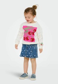 Sweatshirt blanc avec un graphique de cerises roses et vertes, associé à une jupe en denim ornée de petits cœurs roses, et des chaussures slip-on bleues.