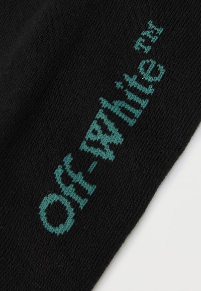 Tissu en maille noire avec texte tricoté en bleu sarcelle "Off-White™" en orientation verticale.