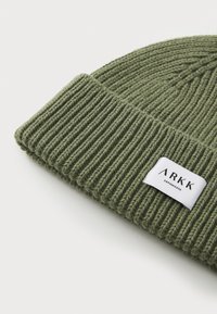 Olive green knit beanie with ribbed texture, featuring a white fabric label with "ARKK" and "Copenhagen" in black lettering.