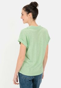 Groene polo met korte mouwen, opgekrulde manchetten, zachte textuur en een relaxte pasvorm. Gecombineerd met denim jeans, bekeken vanuit de rug.