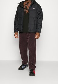 Svart vadderad jacka med huva, kombinerad med en brun tie-dye t-shirt, vinröda manchesterbyxor och svarta sneakers med röda detaljer.