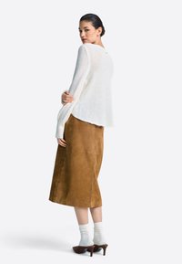 Krem pulover iz pletenine z dolgimi rokavi, kombiniran z rjavo usnjenim midi krilom. Model nosi bele nogavice in rjave čeveljce s peto.