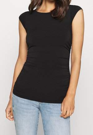 Czarny obcisły top z miękkiej tkaniny z krótkimi rękawkami typu cap i marszczeniami po bokach, zestawiony z jasnoniebieskimi dżinsami.