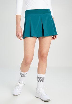 Falda deportiva plisada en color verde azulado con una cinturilla ancha. Combinada con calcetines blancos de Nike hasta la rodilla y zapatillas blancas. Textura de tela suave.