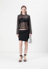 Schwarzes Pailletten-Oberteil mit langen Ärmeln, schwarzer Rock, schwarze Riemchenschuhe und eine silberne Tasche. Schlanker Silhouette mit kontrastierenden Texturen.