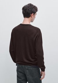 Brauner Pullover mit Rundhalsausschnitt, langen Ärmeln und lässiger Passform. Weiche Textur. Über dunkelgrauen Jeans getragen. Rückansicht, minimales Design.