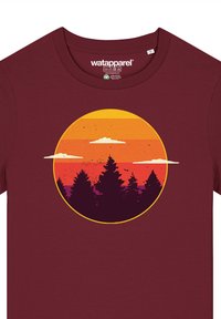 T-shirt bordeaux arborant un graphique circulaire d'un coucher de soleil avec des nuages et des arbres sombres. Le design comprend des rayures horizontales orange et jaunes.