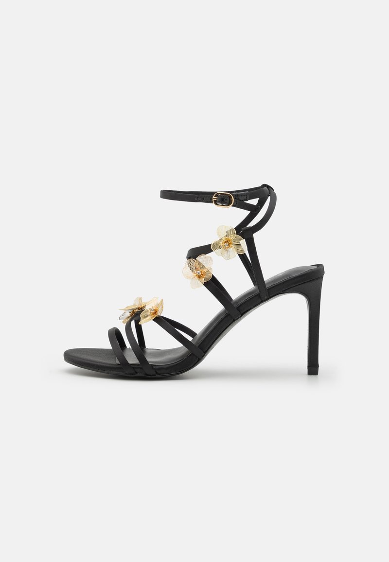 Sandale à talons hauts noire avec des fines lanières et de délicats accents de fleurs dorées, texture élégante ; elle dispose d'une fermeture à boucle sur la lanière de la cheville.