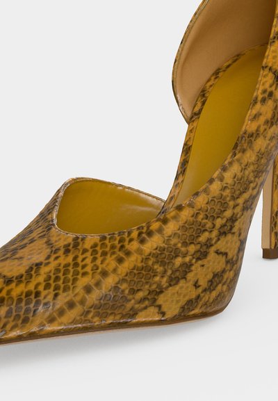 Chaussure à talon haut à bout pointu avec texture de peau de serpent jaune et marron et talon aiguilles fin sur fond blanc.