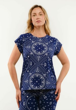 Kvinde iført marineblå kortærmet top og matchende bukser med hvide indviklede paisley- og cirkulære bandanamønstre.