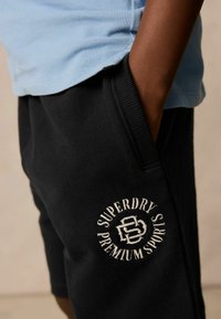 Svarta bomullsshorts med en broderad "Superdry Premium Sports"-logga. Midjan har en subtil ribbad textur.
