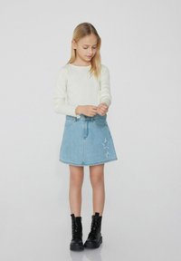 Jupe en denim avec broderie d'étoiles, associée à un haut crème à manches longues avec des poignets festonnés. Des bottes noires à lacets complètent la tenue.