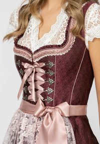 Burgunderfarbendes traditionelles Kleid mit Spitzenakzenten, Satinschleifen und floraler silberner Hardware. Merkmale sind aufwendige Muster und ein mehrlagiger Spitzenrock.