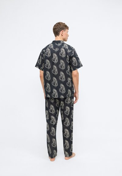 Schwarzes Schlafanzugset bestehend aus einem kurzärmeligen Shirt und langen Hosen, verziert mit einem sich wiederholenden Tigermuster in Beigetönen. Glatte Stofftextur.