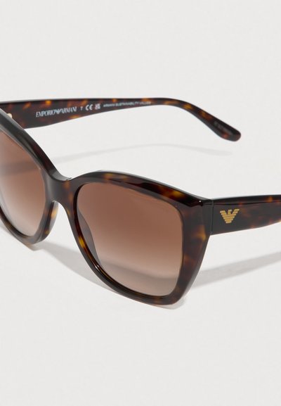 Γυαλιά ηλίου σε σχέδιο τροχιοδρομικού κελύφους με καφέ φακούς διαβαθμισμένου χρώματος. Τετράγωνα πλαίσια με γυαλιστερό φινίρισμα και χρυσό λογότυπο στο πλάι.