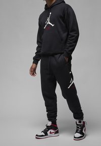 Černá mikina s kapucí s bílým logem Jumpman, doplněná o odpovídající tepláky s logem a černo-červené tenisky.
