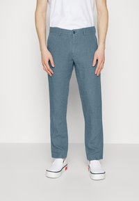 Hellblaue Leinenhose mit geradem Bein, ausgestattet mit einem Knopfverschluss und Gürtelschlaufen, kombiniert mit weißen Turnschuhen.