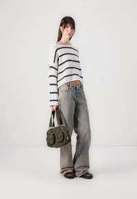 Suéter de punto blanco con rayas marinas, combinado con pantalones vaqueros de pierna ancha en azul desgastado. Bolso verde oliva con dos bolsillos frontales y asas cortas.