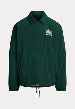 Mørkegrøn knappet jakke med krave, elastiske manchetter, forlommer, snørehætte ved kanten og hvidt broderet emblem på brystet.