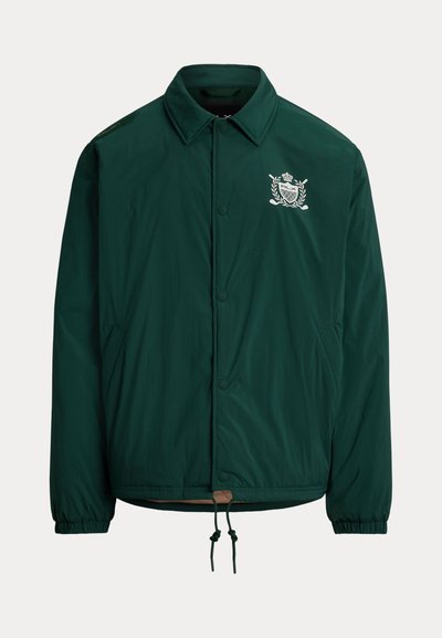 Tume roheline nööpidega jakk kraega, elastsete varrukaotsadega, esimestes taskutes, nööriga äärega ja valge tikandiga vapiga rinnal.